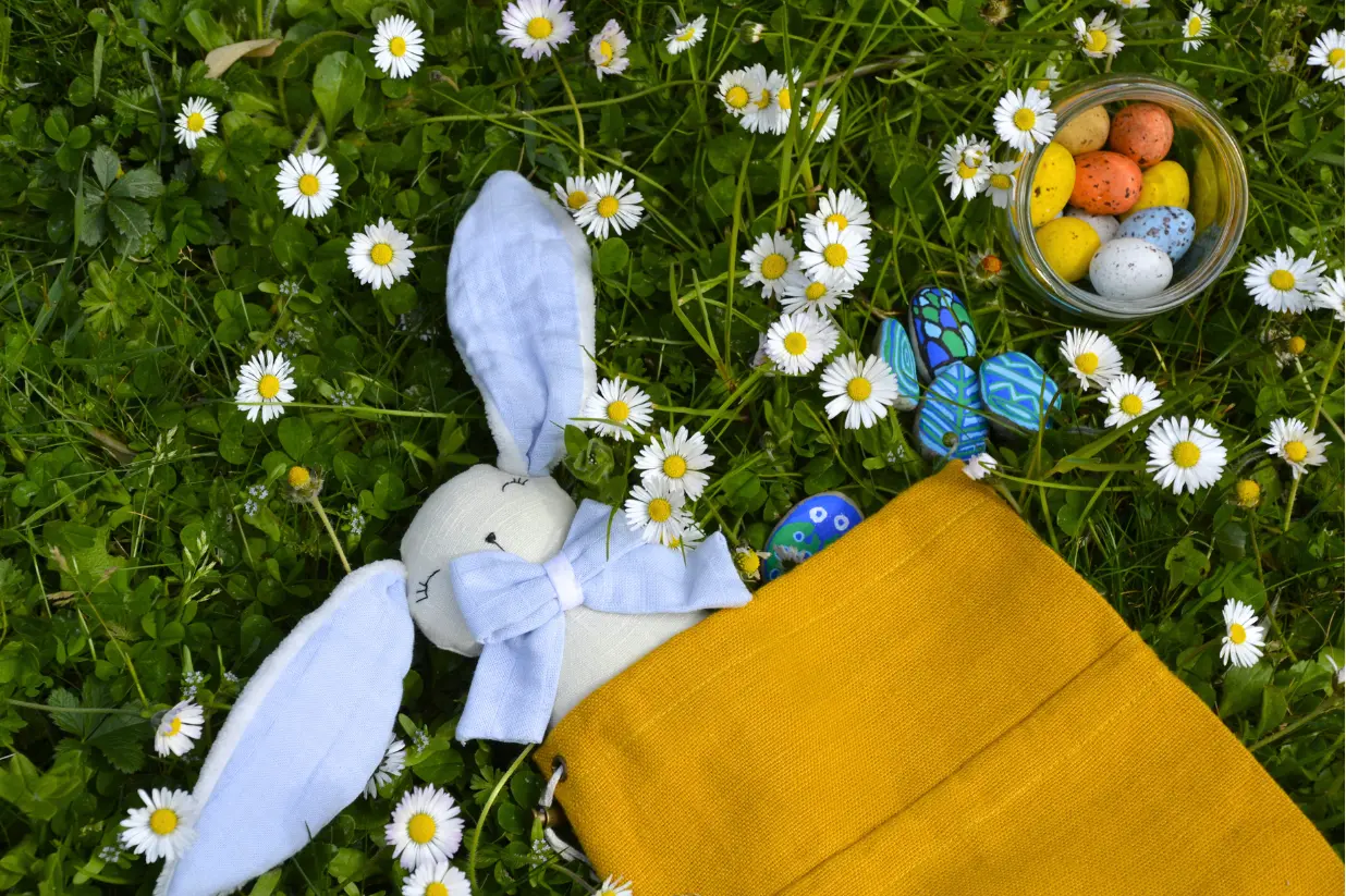 Petit lapin de Pâques en peluche accompagnés de chocolats en vrac dans un bocal en verre et de galets peints