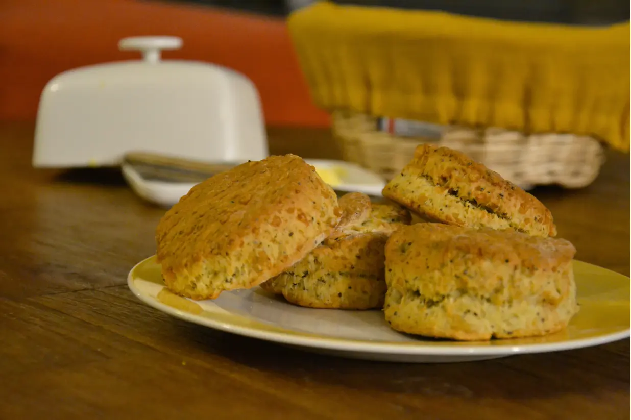 Scones parmesan pavot posés dans une assiette sur une table en bois, avec en arrière-plan un beurrier et une corbeille à pain jaune les extra-ordinaires