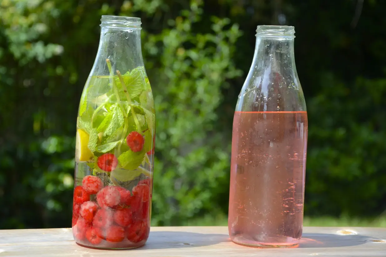 Eau fruitée à la framboise, 1 bouteille contenant tous les ingrédients infusés, 1 bouteille montrant l'eau parfumée une fois filtrée